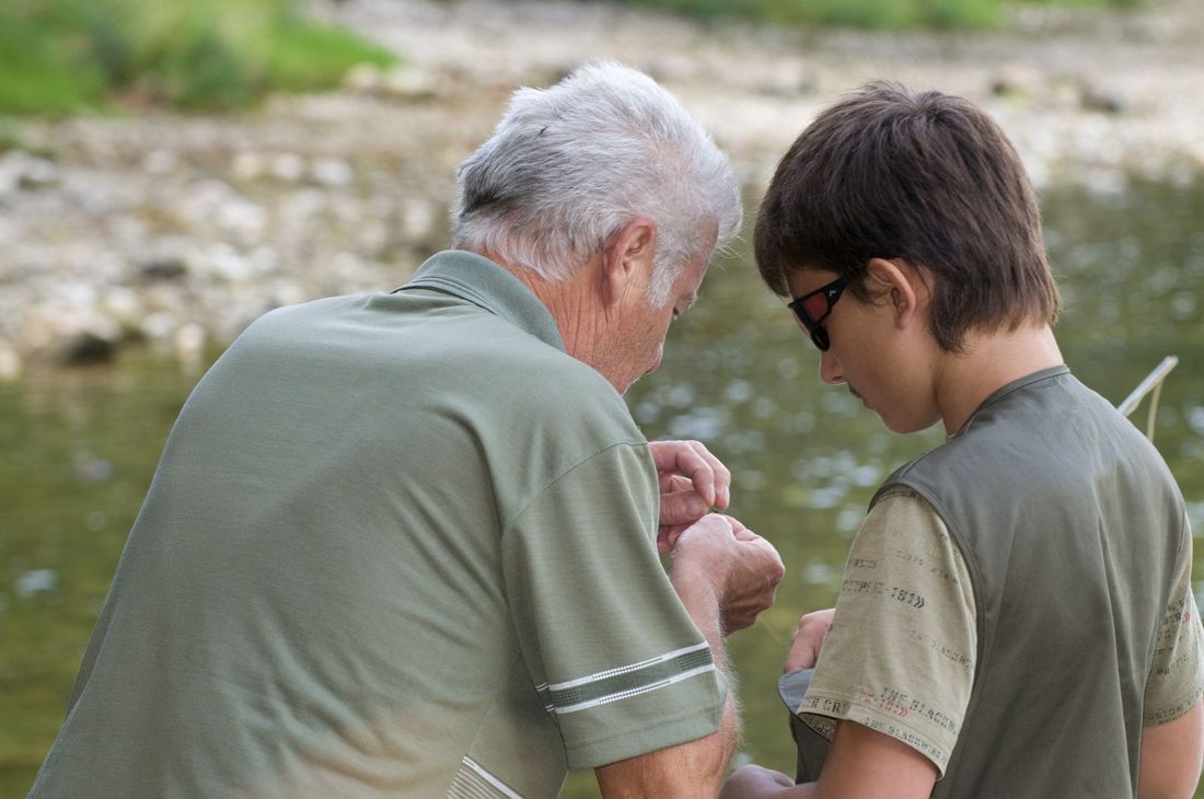 Ein älterer Fischer zeigt einem Buben am Fluss, wie man einen Köder bindet